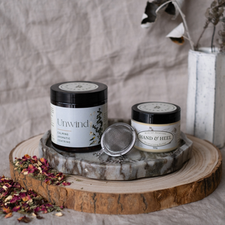 Two jars labeled 'Unwind' and 'Hand & Heel' on a wooden surface with a neutral background.